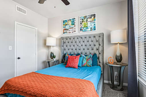 A bedroom with a blue bedspread and a grey tufted headboard.