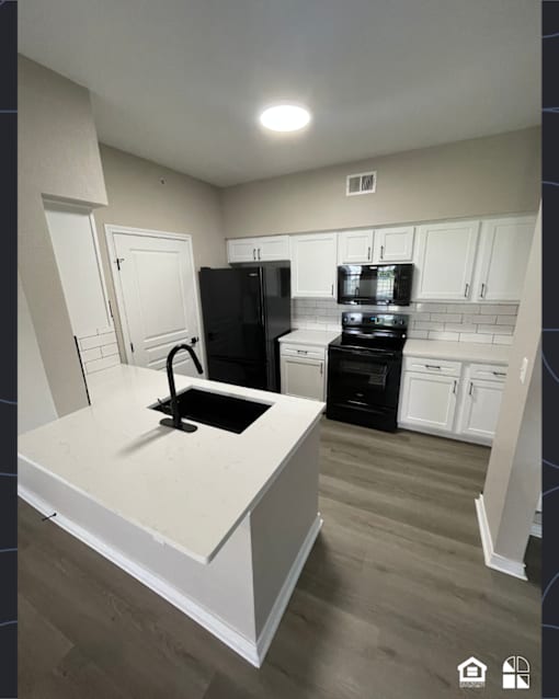 A kitchen with a black fridge and stove top oven.