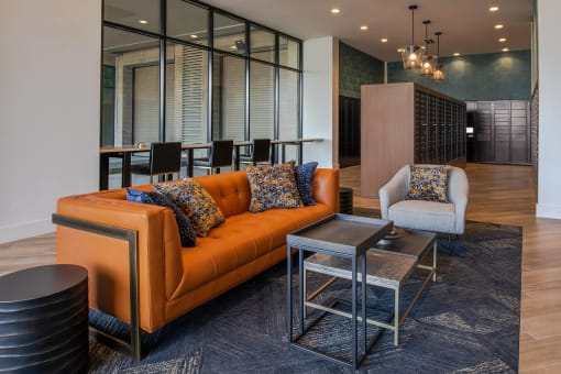 seating area with orange couch, white chair, and various sizes of side tables on a gray rug at The Apex at CityPlace, Overland Park