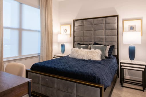 a bed with blue comforter in a bedroom with two lamps and a large window at The Apex at CityPlace, Overland Park, 66210