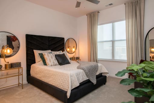 bedroom with a large window, two nightstands with mirrors, and a bed with white comforter at The Apex at CityPlace, Overland Park, Kansas