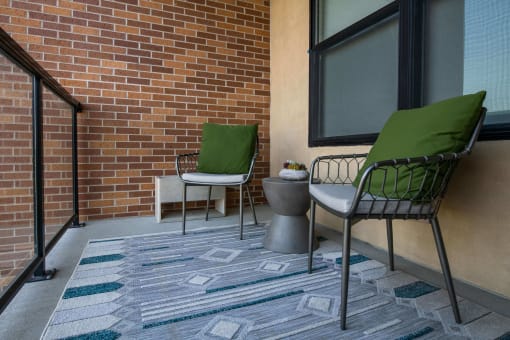 the balcony of an apartment with two chairs and a rug looking over a glass railing at The Apex at CityPlace, Kansas