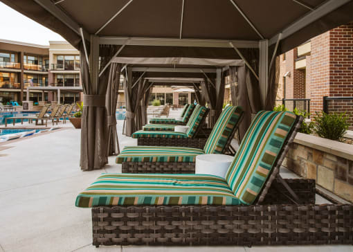 chaise lounge chairs in a row under a canopy next to an outdoor pool  at The Apex at CityPlace, Overland Park, Kansas