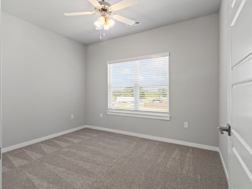 an empty bedroom with a large window and a ceiling fan at Hillcrest Village, Springdale, AR