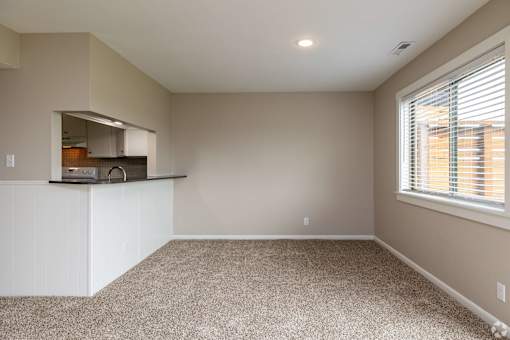 A spacious room with a window and a kitchen area in the background.