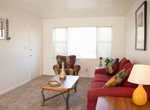 A living room with a red couch, a wooden coffee table, and a lamp at North Village Apartments in Kansas City, MO.