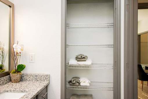 A bathroom with a large mirror, a sink, and a shelf with towels and toiletries.