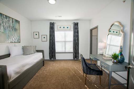 A bedroom with a bed, desk, chair, and a painting on the wall.