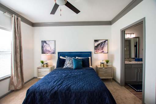 A bedroom with a blue bedspread and a ceiling fan.