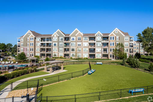 an exterior view of an apartment building with a green field and a tennis court  at Waterside Residences on Quivira, Lenexa, Kansas