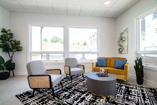 A living room with a grey ottoman, two chairs and a sofa.