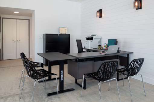 A black desk with four chairs and a laptop on it.