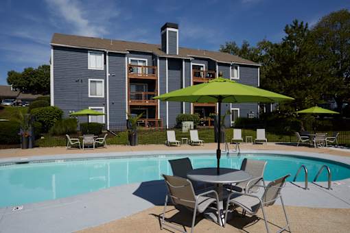 A pool with chairs and umbrellas in front of a grey building.