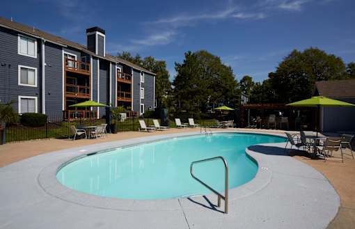 A swimming pool in front of a building with a green lawn.