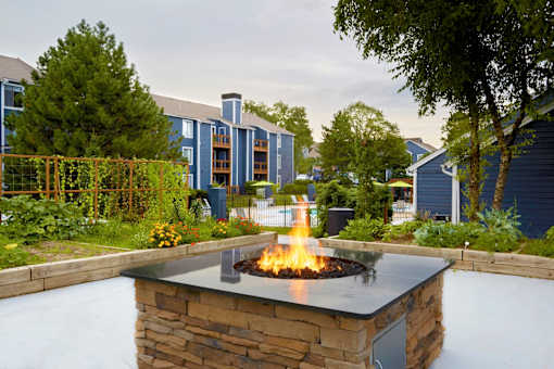 A fire pit in the middle of a garden with a building in the background.