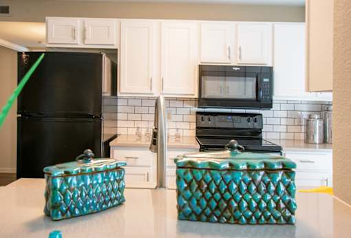 A black refrigerator and microwave in a kitchen with white cabinets.