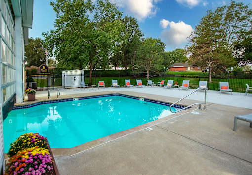 A pool surrounded by trees and chairs.