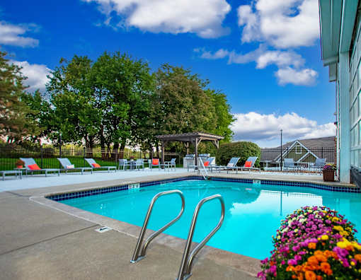 A pool with a diving board and chairs around it.