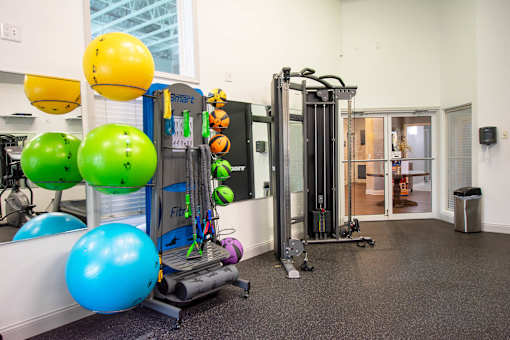 A gym with a variety of equipment including a treadmill, exercise balls, and a weight machine.
