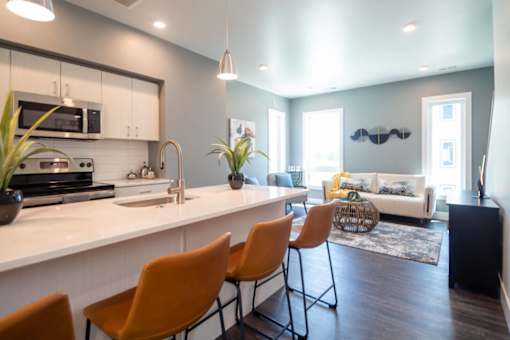 A modern kitchen with white countertops and orange chairs.