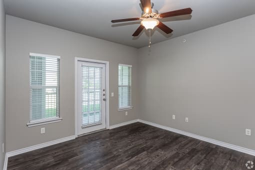 an empty living room with a ceiling fan and windows