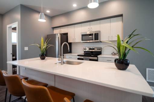 A modern kitchen with a white countertop and orange chairs.