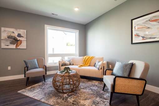 A living room with a grey couch, a yellow throw, and a woven chair.