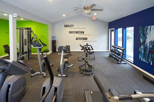 A gym with a green wall and a sign that says "Ability Motivation Attitude".