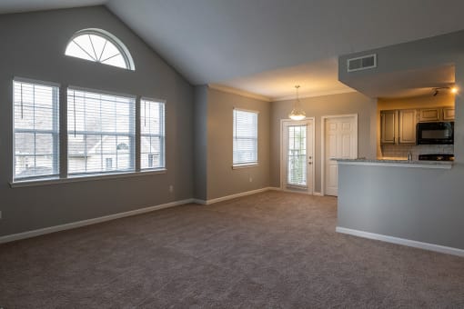 an empty living room with a kitchen in the background