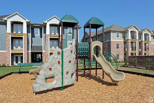 A playground with a slide and a climbing structure in front of apartment buildings.