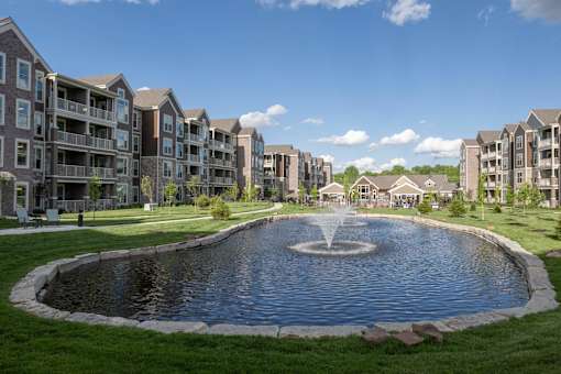 a large pond with a fountain in front of an apartment building at The Clearing at ONE28, Olathe
