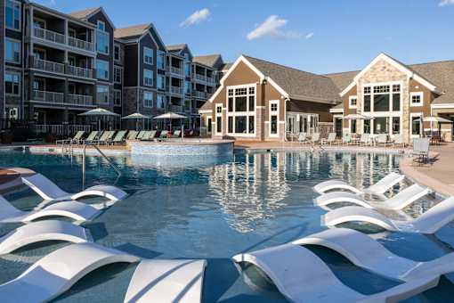 a large pool with white chairs in front of an apartment building at The Clearing at ONE28, Olathe, 66062