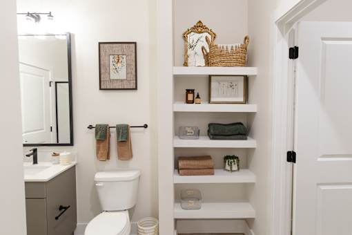 A bathroom with a toilet, sink, and shelves with towels and other items.