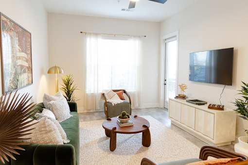 A living room with a green couch, a wooden coffee table, and a flat-screen TV mounted on the wall.