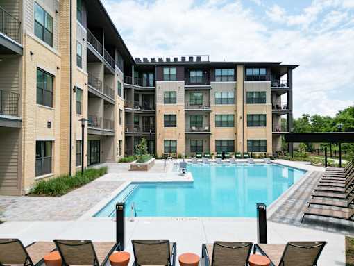 A large swimming pool surrounded by lounge chairs and apartment buildings.