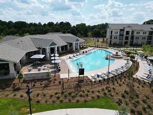 A large outdoor swimming pool surrounded by a black fence and a building in the background at The Crest at South Point Apartments, Georgia, 30253