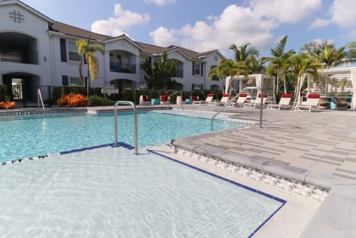 A swimming pool surrounded by a tiled floor and lounge chairs. at The Crest at Laurel Canyon Apartments, Naples, FL