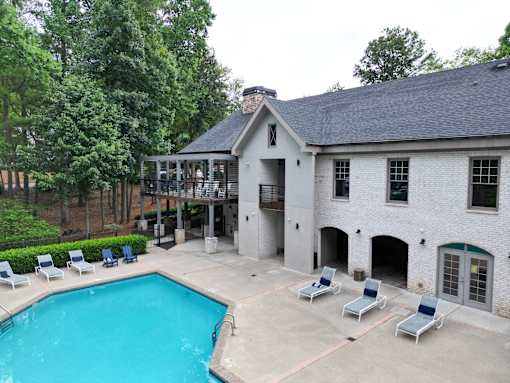 A pool and loungers in front of a white building with a black roof.