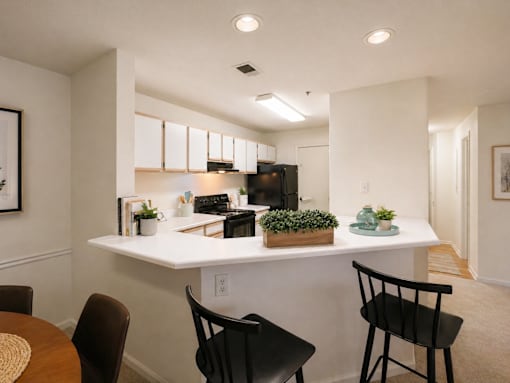 A kitchen with a white countertop and black chairs.