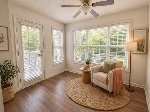 A room with a ceiling fan, a chair, and a table with a potted plant.