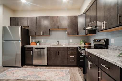 A kitchen with dark brown cabinets and a patterned rug on the floor.