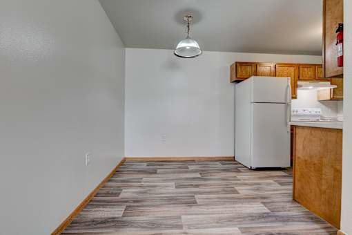 an empty living room with a kitchen with a refrigerator