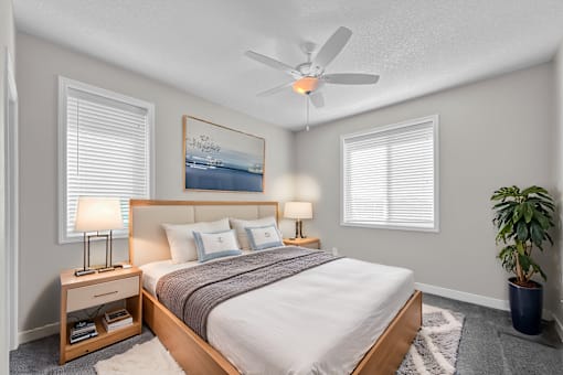 A bedroom with a bed, two lamps, a ceiling fan, and a potted plant.