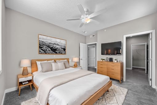 A bedroom with a large bed, a ceiling fan, and a painting on the wall.