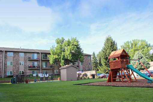 A playground with a wooden structure and a green slide in front of a building.