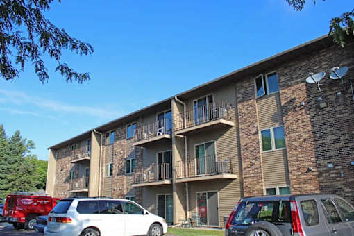 A large apartment building with a white van and a red truck parked in front.