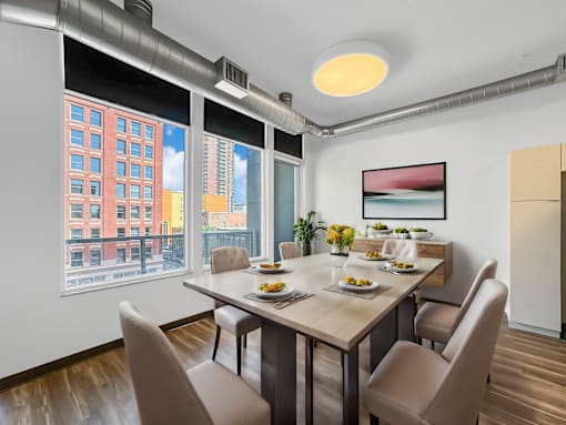 A dining room with a table set for four and a view of a cityscape through the windows.