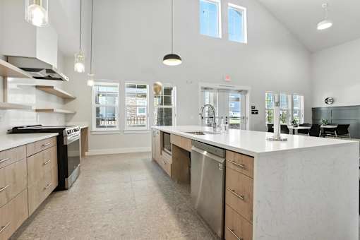 A modern community room with kitchen with a large island and stainless steel appliances.