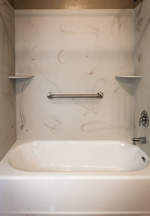 A white bathroom with a marble style wall and a white bathtub.