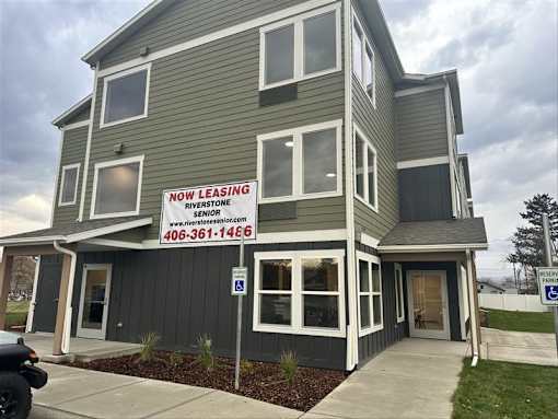 A two-story building with a sign that says "NOW LEASING" and a website address.